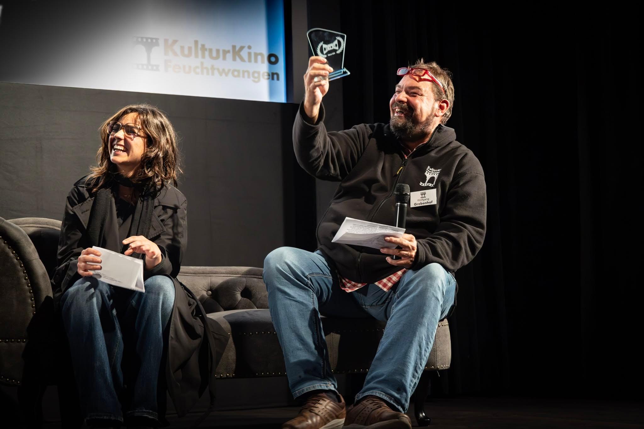 Award ceremony at KulturKino Feuchtwangen, the host laughing and holding up the trophy